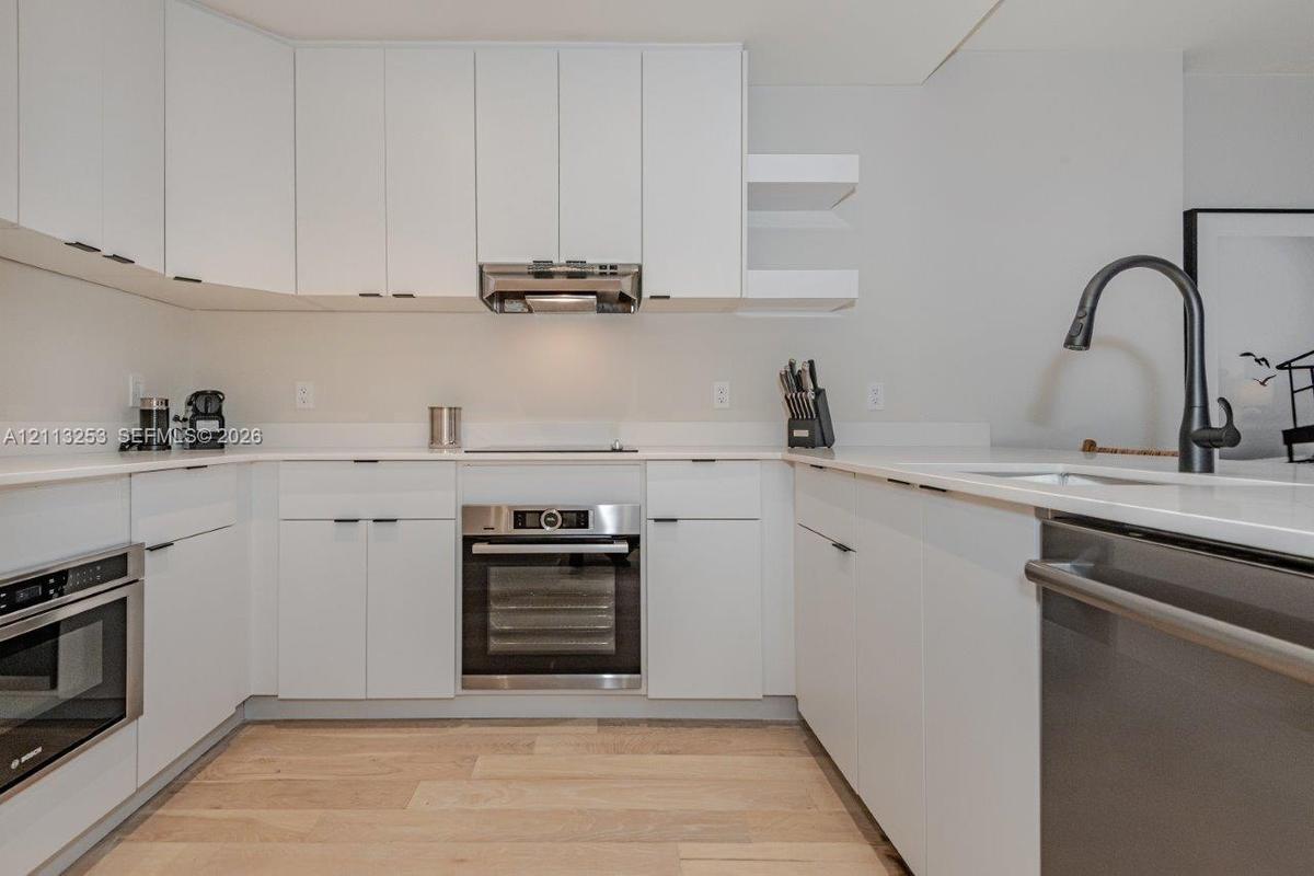 Kitchen featuring white flat-panel cabinetry, stone countertops, stainless steel appliances, a matte black high-arc faucet, and wood-finish flooring