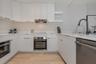 Kitchen featuring white flat-panel cabinetry, stone countertops, stainless steel appliances, a matte black high-arc faucet, and wood-finish flooring