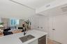 Kitchen island featuring a solid-surface countertop, stainless steel undermount sink, and matte black faucet, complemented by wood-finish flooring and