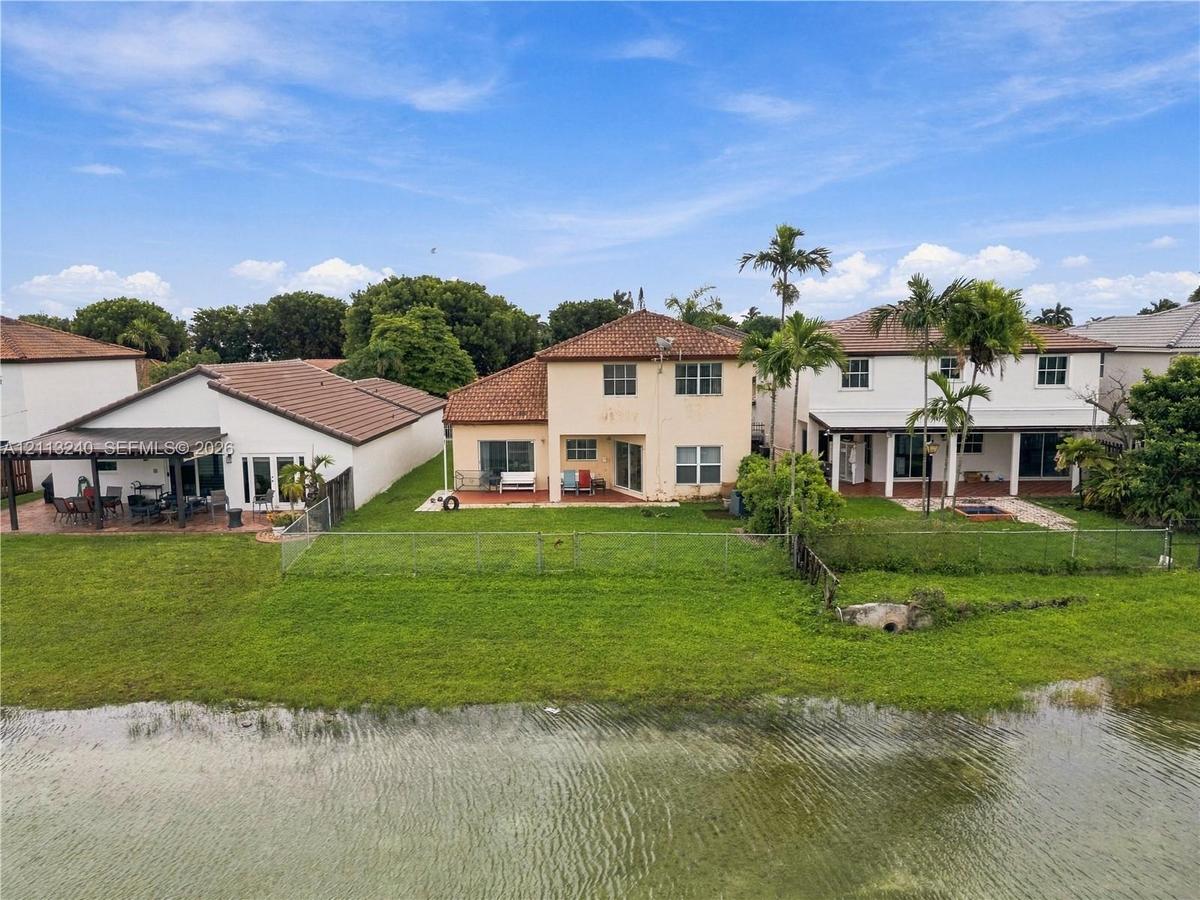 Two-story residence featuring a tile roof, covered rear patio, chain-link fencing, and direct water frontage on a landscaped lot