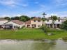 Two-story residence featuring a tile roof, covered rear patio, chain-link fencing, and direct water frontage on a landscaped lot