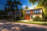 Modern two-story architectural exterior featuring stone facade, wood-finish paneling, expansive glass windows, integrated recessed lighting, and a pri
