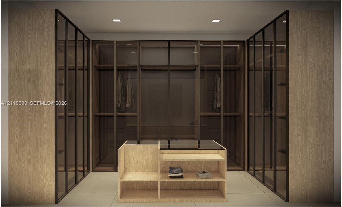 Custom dressing area featuring floor-to-ceiling cabinetry with glass-panel doors, integrated shelving, and a central built-in island with a countertop