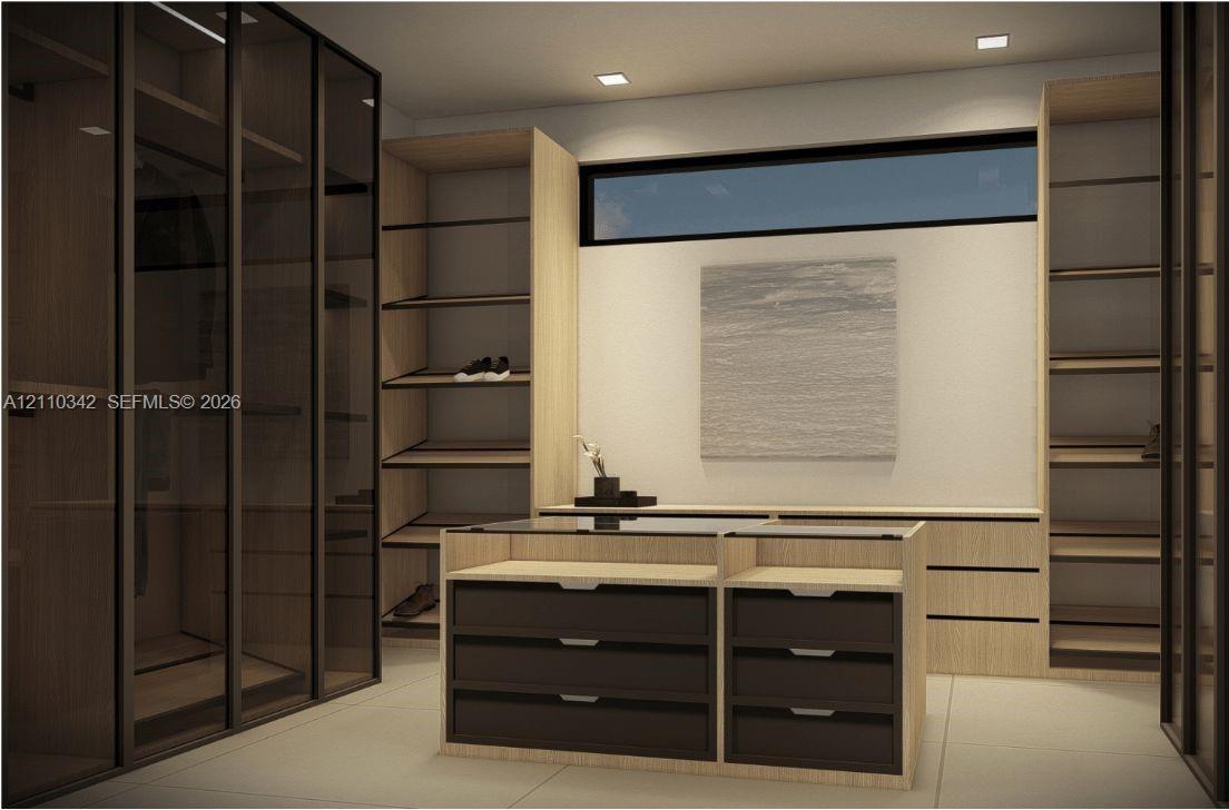 Custom cabinetry featuring wood-finish shelving, glass-front wardrobe enclosures, a central island with a glass top and matte-finish drawers, and rece
