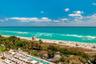 Direct oceanfront exposure featuring a swimming pool, glass-panel perimeter fencing, lush perimeter landscaping, and mature palm trees
