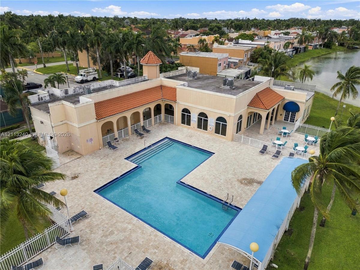 L-shaped swimming pool featuring an expansive paved deck, covered loggias, and clay tile roof accents