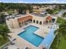 L-shaped swimming pool featuring an expansive paved deck, covered loggias, and clay tile roof accents