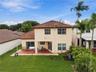Two-story exterior featuring a clay tile roof, stucco facade, covered rear patio, and expansive lawn with mature palm trees