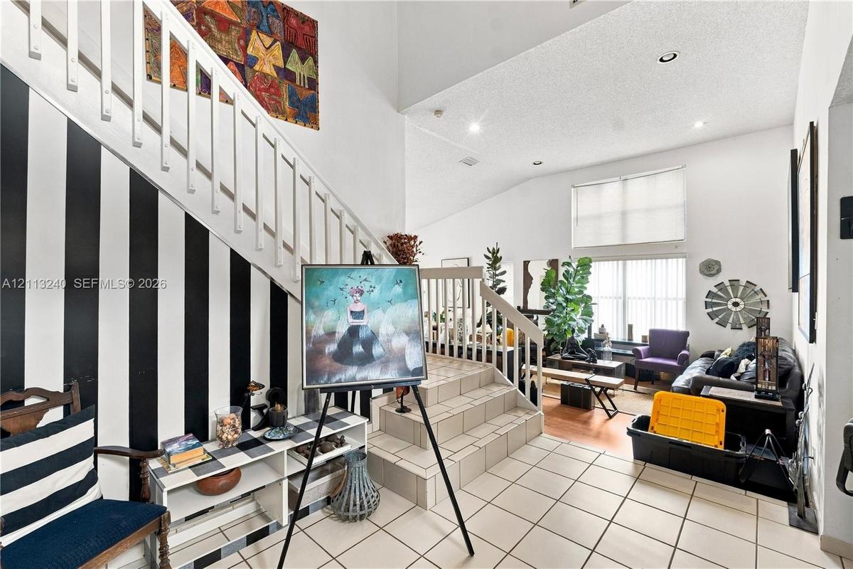 High-ceiling interior featuring a tiled staircase with white railings, ceramic tile flooring, and recessed lighting