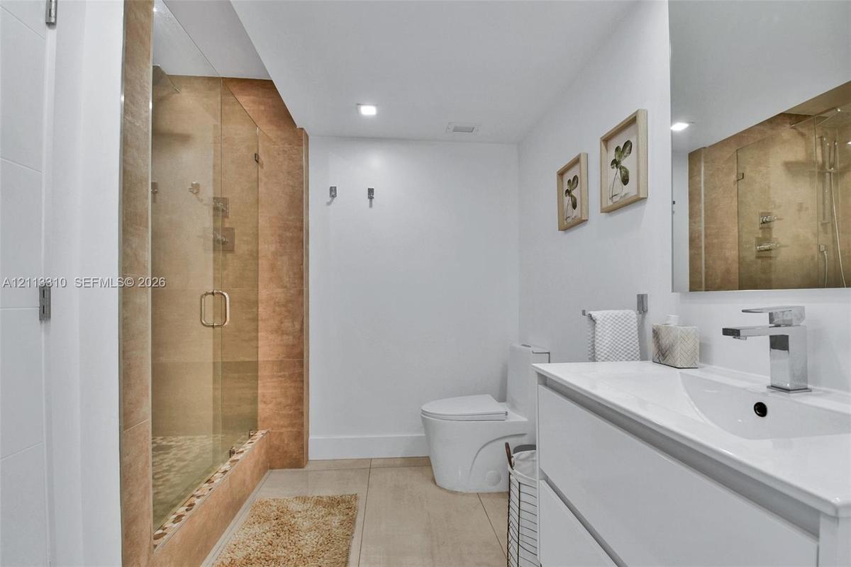 Bathroom featuring a glass-enclosed walk-in shower with textured wall tile, a white vanity with an integrated basin, a polished chrome faucet, and a w