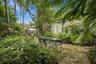 Private backyard featuring flagstone hardscaping, mature tropical landscaping, a built-in greenhouse, and a white exterior structure with glass-paned 