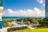 Outdoor amenity area featuring a swimming pool, expansive lawn, mature palm trees, and horizon-spanning ocean waters