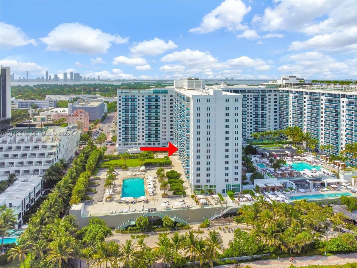 Aerial perspective of high-rise residential building featuring multiple swimming pools, expansive sun decks, manicured landscaping, and mature palm tr