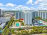 Aerial perspective of high-rise residential building featuring multiple swimming pools, expansive sun decks, manicured landscaping, and mature palm tr