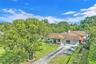 Single-story residence featuring a multi-gabled shingle roof, expansive front lawn, mature trees, and a paved driveway