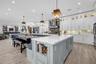 Kitchen featuring shaker-style cabinetry with glass-panel upper doors, a large central island with integrated storage, white quartz countertops, wood-