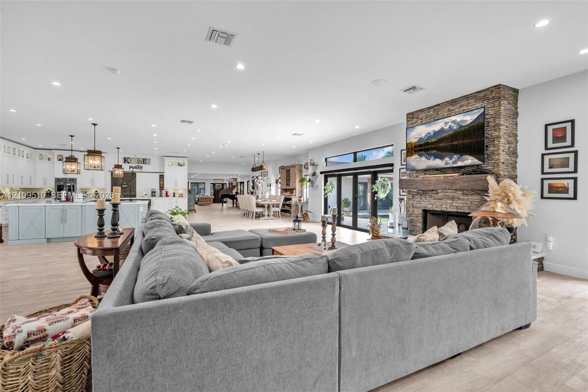 Open-concept living area featuring stacked stone fireplace, distressed timber mantel, wood-finish flooring, recessed lighting, and multi-panel sliding