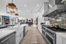Kitchen featuring white cabinetry, quartz countertops, a farmhouse sink, stainless steel professional-style range with matching hood, and multi-tone s
