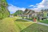 Expansive rear exterior space featuring a manicured lawn, paved concrete walkways, mature palm trees, and an exterior structural awning