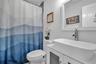 White vanity with a rectangular vessel sink and chrome-finish faucet, paired with a large framed mirror and a tile-surround shower
