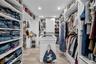 Walk-in closet featuring floor-to-ceiling white built-in shelving, a central storage island with a surface inlay, recessed lighting, and tile flooring