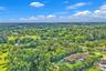 Aerial perspective of a sprawling property featuring mature trees, lush landscaping, a wide-reaching lot, and a residence with a multi-hipped roofline