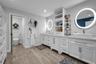 Dual-vanity cabinetry with white finishes, vessel sinks, quartz countertops, integrated shelving, and illuminated circular mirrors