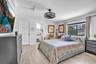 Light-filled bedroom featuring wood-finish flooring, a drum-style caged ceiling fan, and a wide window with integrated curtain rod hardware
