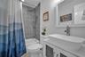 Bathroom featuring a white vessel sink with a chrome faucet, wall-mounted mirror with a white frame, shower with grey tile surround, adjustable handhe