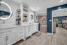 Dual white vanities featuring vessel sinks, integrated shelving, lighted circular mirrors, and a walk-in glass-enclosed shower with stone-tile surroun