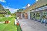 Spacious concrete patio featuring a built-in masonry outdoor fireplace, large glass multi-panel doors, and direct access to an expansive synthetic tur