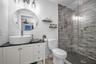 Bathroom featuring a white vanity with a dark countertop, a vessel sink, an oval wall-mounted mirror, and a walk-in shower with textured tile surround