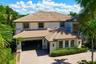 Two-story stucco exterior featuring a multi-hipped tile roof, paver driveway, multi-car garage, and grid-pattern window panes
