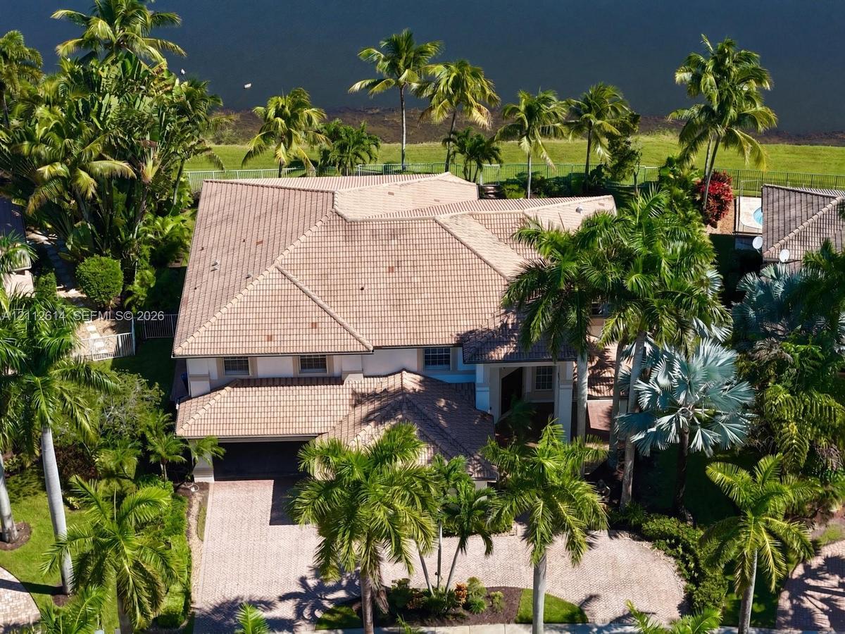 Multi-level residence featuring a tile roof, paved driveway, and mature landscaping on a waterfront lot