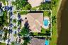 Aerial perspective of a property featuring a tile roof, an integrated swimming pool with a spa, paver hardscaping, and waterfront positioning