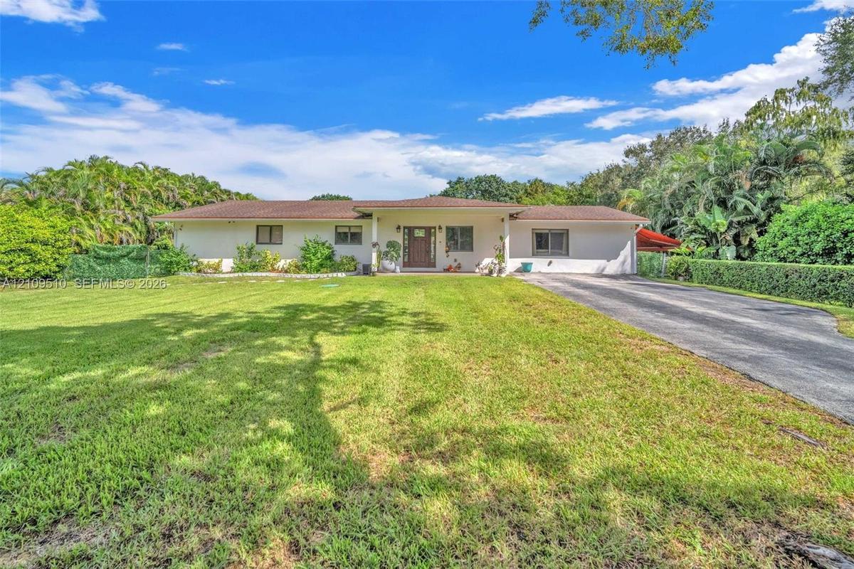 Single-story ranch exterior featuring a light-toned stucco façade, a covered entryway, a hipped shingle roof, and a paved driveway