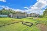 Expansive backyard featuring artificial turf, a permanent greenhouse structure, a covered patio with integrated privacy screens, and a timber-framed g