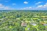 Aerial perspective featuring expansive acreage, mature tree canopy, residential structure with a shingled roof, and vast green space