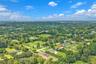 Aerial perspective of a sprawling property featuring a hip-roof residence, expansive grounds, mature landscaping, and significant perimeter vegetation