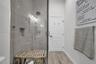 Walk-in shower featuring oversized tile walls, a recessed wall niche, a ceiling-mounted rainfall shower head, and a frameless glass door, complemented