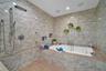 Walk-in wet room featuring textured tile walls, a deep soaking tub with chrome hardware, an integrated shower system with a handheld sprayer, built-in