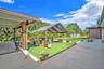 Covered patio with wood-post supports, expansive artificial turf grounds, and concrete paved perimeter