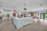 Open-concept kitchen featuring an expansive center island with stone countertops, white cabinetry, integrated stainless steel appliances, and wood-fin