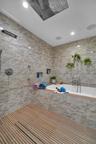 Wet room featuring a deep soaking tub, ceiling-mounted rainfall showerhead, linear floor drain, wood-slat flooring, and textured tile wall cladding