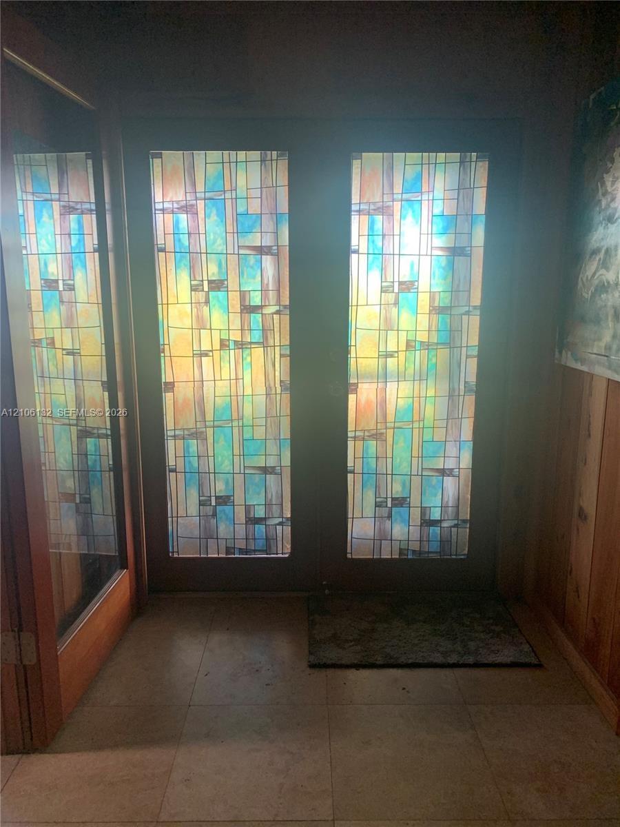 Double entry doors featuring geometric stained-glass inserts, vertical wood paneling, and tile flooring