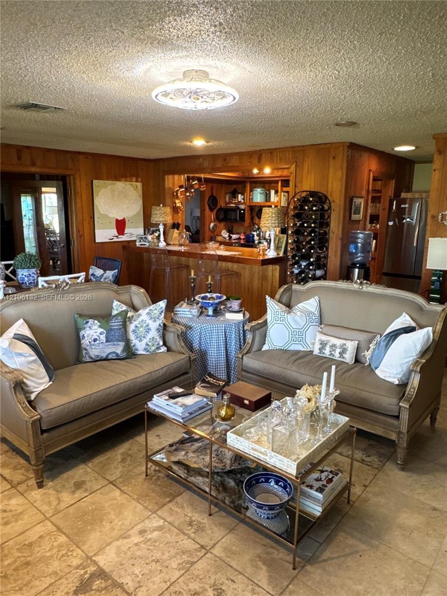 Living area featuring warm wood-paneled walls, neutral stone-finish flooring, and a built-in wooden bar with integrated cabinetry