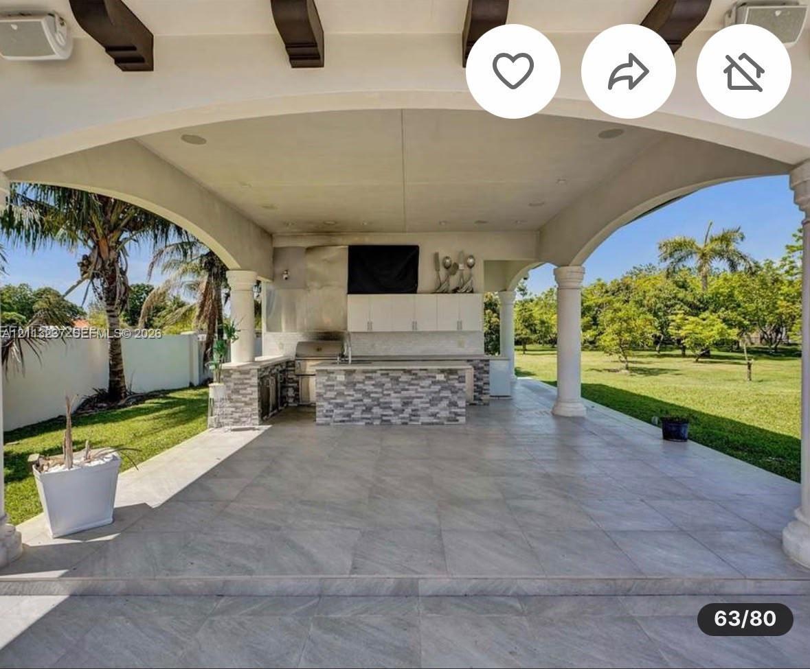 Covered outdoor kitchen featuring tile flooring, exposed decorative ceiling beams, stone-finished cabinetry, a stainless steel grill, and arched archi