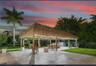 Outdoor living area featuring a large thatched-roof palapa, expansive stone-tile patio, and mature landscaping