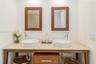 Double vanity featuring dual vessel sinks, stone-surface countertop, wood-finish console base, and paired wall-mounted wooden mirrors