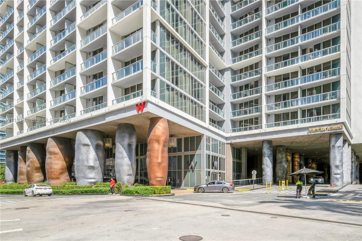 High-rise exterior featuring a multi-story glass facade, private glass-railed balconies, and distinctive sculpted structural columns at the building e